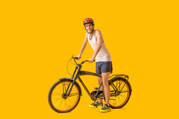 Young male cyclist with bicycle on yellow background