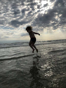 A silhouette of a kid jumping on a beach in a water