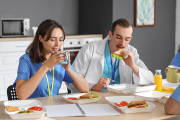 Female doctor having lunch with her colleagues at table in hospital kitchen