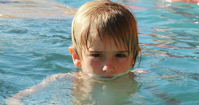 Child inside swimming pool water looking to camera, water splashing