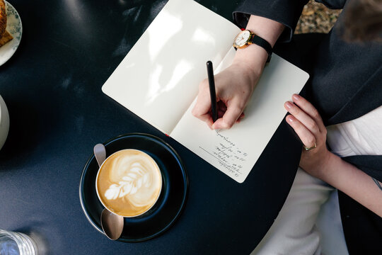 Crop female taking notes in notebook at table in cafe