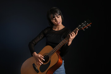 Cool young woman playing guitar on black background
