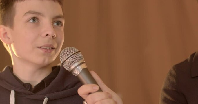 Close-up teenage student speaks into microphone during school debate. 7th grader confidently expresses opinion. Talking boy showcasing budding eloquence and critical thinking skills on stage in school