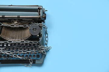 Vintage typewriter with chains on blue background. Printing ban concept