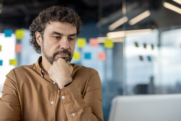 Pensive Hispanic businessman deeply focused and contemplating while in a modern office setting,...