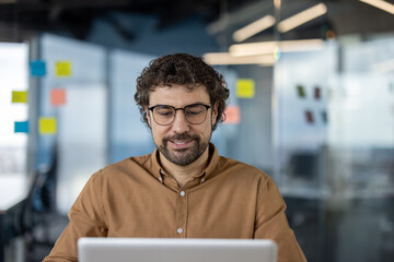 Professional male entrepreneur with glasses using computer in a contemporary office setting, reflecting productivity and focus.