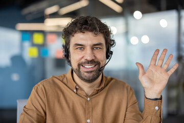 Portrait of a cheerful male customer service representative wearing a headset and waving in a...