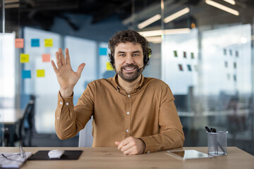 Cheerful male professional with headset greeting in a contemporary office space with bright,...