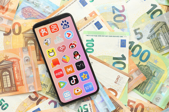 KYIV, UKRAINE - APRIL 1, 2024 Asian apps icon on smartphone screen on many euro money bills. iPhone display with app logo with european currency euro banknotes
