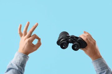 Male hands with binoculars showing OK on blue background