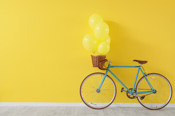 Bicycle with balloons in basket on yellow background