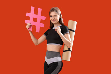 Sporty female coach with yoga mat and hashtag sign against color background