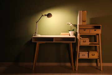 Comfortable table with glowing lamp, houseplant and books in evening