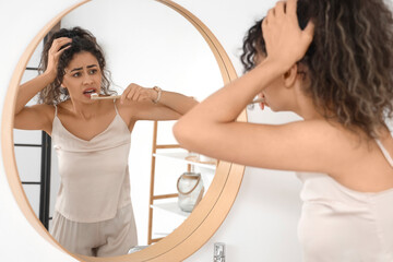 Hurrying young African-American woman brushing teeth near mirror in bathroom