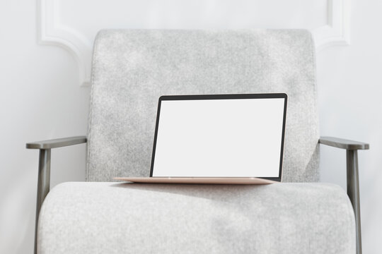 Laptop with empty screen on chair in sunlit living room. Mock up