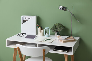 Comfortable workplace with tablet computer, hourglass and notebooks near green wall