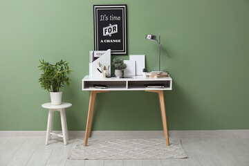 Comfortable workplace with tablet computer, desk lamp and notebooks near green wall