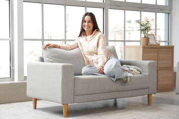 Pretty young woman sitting on grey sofa in living room - 777738615