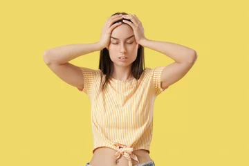 Schilderijen op glas Tired young woman suffering from headache on yellow background © Pixel-Shot