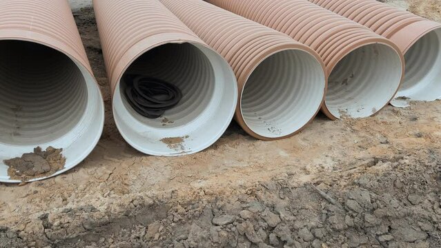 Corrugated Double-Walled Polypropylene Pipes Lined Up at a Construction Site During Daytime. Several large red corrugated plastic pipes on a dirt ground, likely for drainage or utilities.
