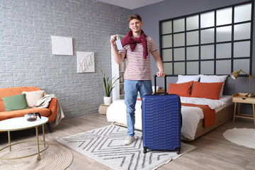Male tourist with door hanger and suitcase in hotel room