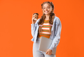 Happy smiling young woman with braids holding laptop and cup of coffee on orange background - obrazy, fototapety, plakaty