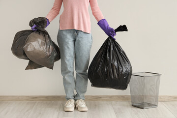 Woman with garbage bags and trash bin near white wall