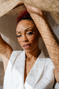 African American young woman covering face with jute curtain in studio