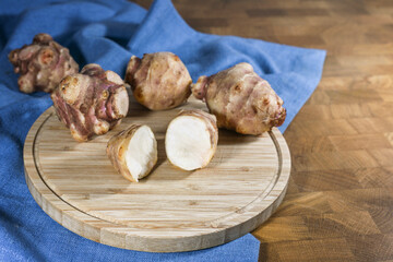 Root vegetable Jerusalem artichoke or topinambur (Helianthus tuberosus), whole and halved on a rustic wooden kitchen board and a blue napkin, for healthy diet and diabetes, copy space