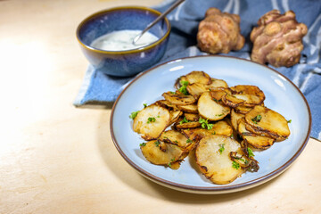 Crispy fried slices of Jerusalem artichoke or topinambur (Helianthus tuberosus) with onions and parsley on a blue plate with a fresh dip, healthy root vegetable, copy space