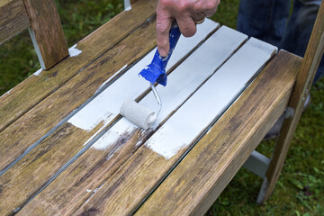 Painting a weathered wooden garden bench with a white diffusion-open weather protection coat using a paint roller, preparation for the outdoor season, copy space