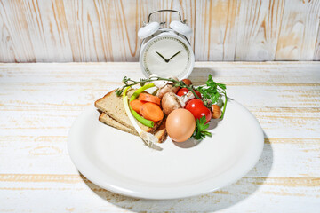Interval fasting diet concept symbolized by a plate filled to one third with food and an alarm clock on a light wooden background, healthy and lasting weight loss, copy space, selected focus