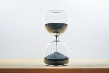 Hourglass with black sand on a wooden table against a light gray background, concept for time passing by, seize the day and enjoy the moment, copy space - 777745477