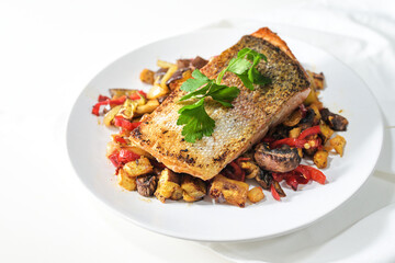 Rain trout fillet with a crispy fried skin on vegetables from the oven and parsley garnish served on a white plate, healthy fish dish suitable for low carb diet, copy space