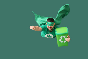 Young man dressed as eco superhero flying with garbage bin on green background. Ecology concept