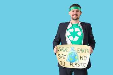 Young man dressed as eco superhero holding poster with text SAVE EARTH SAY NO TO PLASTIC on blue background. Ecology concept - obrazy, fototapety, plakaty
