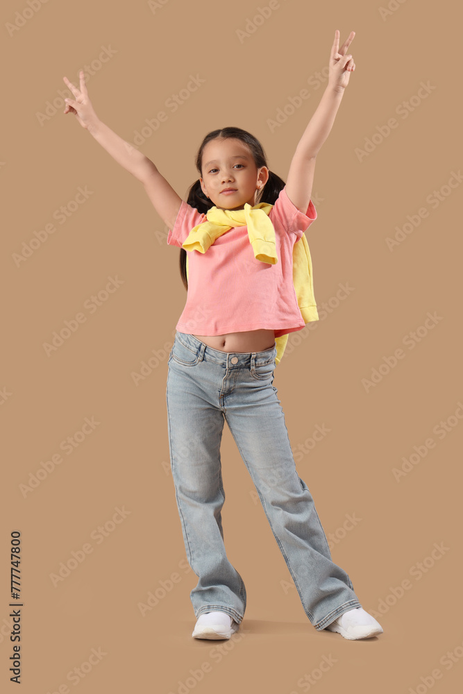 Poster Portrait of fashionable little girl showing victory gestures on beige background