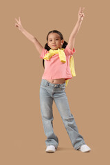 Portrait of fashionable little girl showing victory gestures on beige background