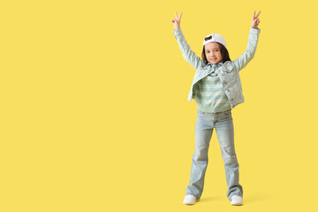 Portrait of fashionable little girl showing victory gestures on yellow background