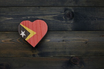wooden heart with national flag of east timor on the wooden background.