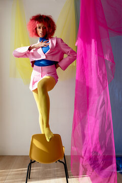 Black female in stylish pink outfit on chair in studio