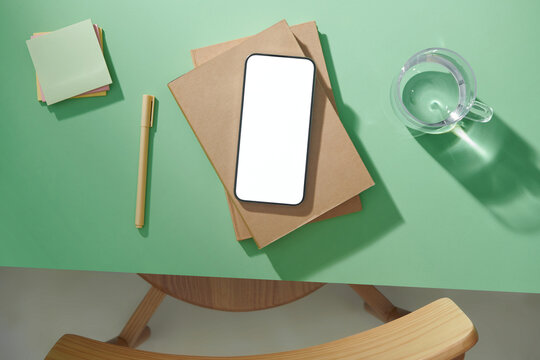 Office desk with sticky note, smartphone, notepad and cup of water.