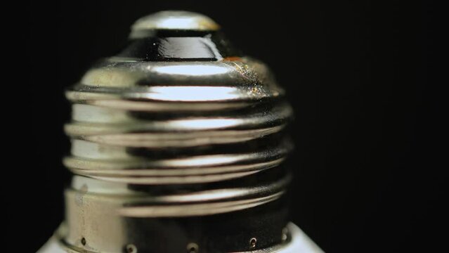 Macro close up of light bulb socket base. Screw base of the bulb rotation with shallow depth of field and black background. Metal screw-in Edison bayonet socket extender or lamp connector.
