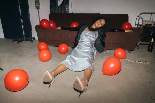 Elegant Woman Seated on Floor by Sofa with Red Balloons