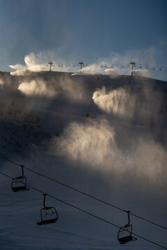 Snow makers shoot artificial snow at sunrise