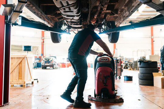 Mechanic under the chassis of a car during cleaning.