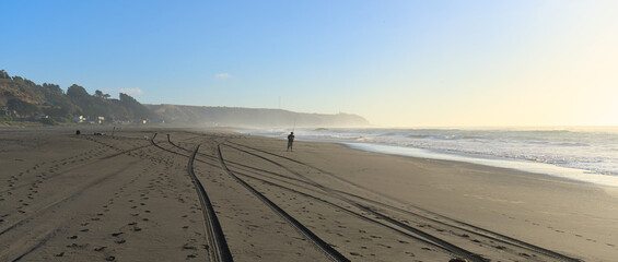 Person walking in the distance on Sand beach during windy summer day on pacific ocean (Iloca, Chile)
