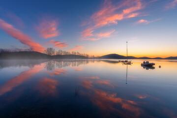 A spring peaceful blue hour before sunrise with beautiful red cloud reflections and silhouettes of...