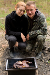 two people look at meat on fire. grill, picnic in the forest
