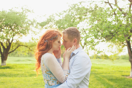 young couple in love kissing. woman with fiery hair in a blue dress. photo shoot in the garden